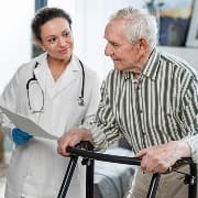 A care professional assisting an older man with a walking frame