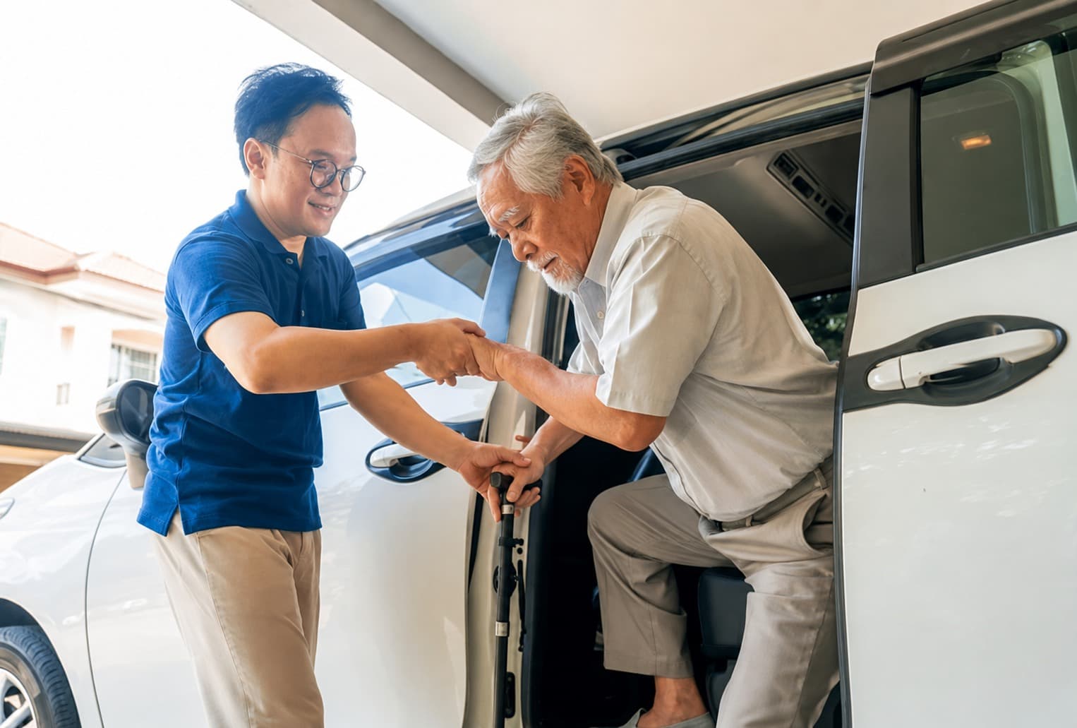 A support worker helping an older man step out of a vehicle